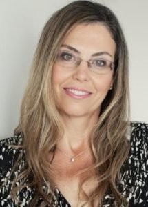 A woman with long hair wearing glasses and smiling.